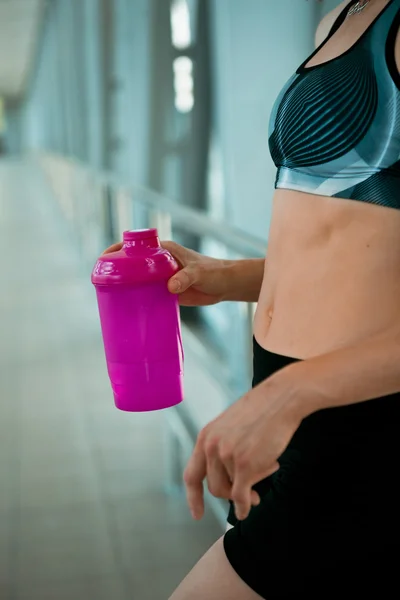 Woman holding bottle of water, taking a break from exercise.