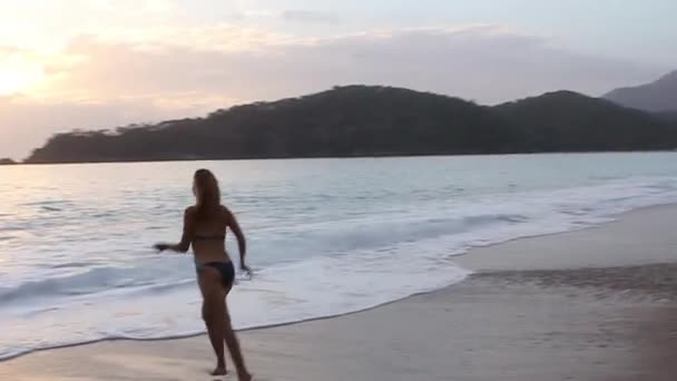 Young happy woman in blue swimwear running into the sea on sunset sky,  rising water splashes — Stock Video