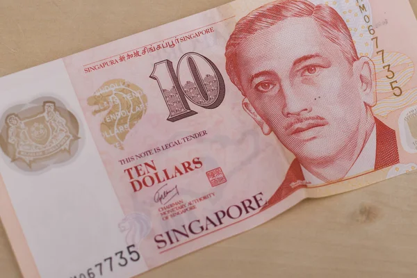 Currency of the Singapore - One red ten dollar note spread out on a light brown background. Money exchange.