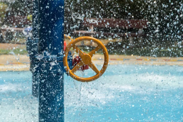 Children\'s water park spray splash pad looking to turning wheel in the sunshine and water spray.