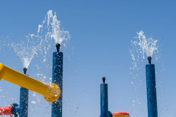 Summertime fun for the kids at the splash pad to play with water falling from bright colored fountains to blue sky.