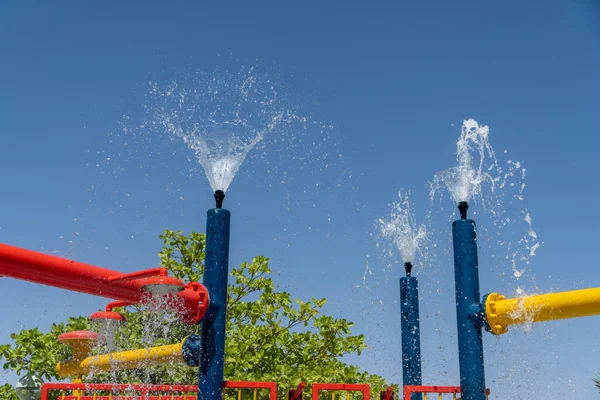 三台蓝色喷水公园洒水洒水器在孩子们的头顶上 让孩子们享受夏日的欢乐 — 图库照片