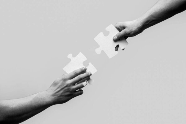 Two hands trying to connect couple puzzle. Closeup hands of man connecting jigsaw puzzle. Business solutions, success and strategy concept. Black and white