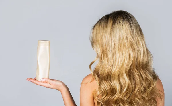 Woman hold bottle shampoo and conditioner. Woman holding shampoo bottle. Beautiful blonde girl with a bottle of shampoos in hands. Girl with shiny and long hair. Woman long hair — Stock Photo, Image