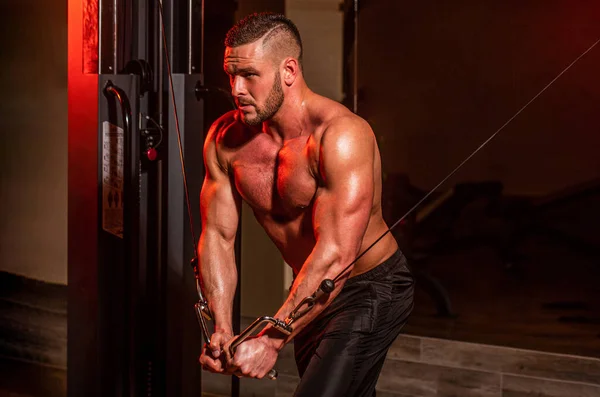 Fitness man execute exercise with exercise-machine Cable Crossover in gym. Handsome man with big muscles in gym. Machine in the gym. Muscular man working out in gym doing exercises at triceps, strong