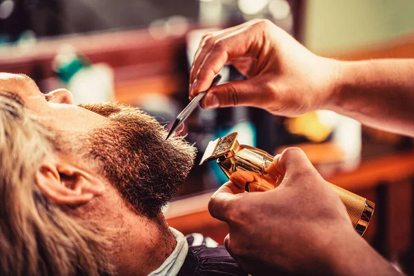 O barbeiro trabalha com um cortador de barba. Um cliente Hipster a cortar o cabelo. Mãos de um cabeleireiro com um cortador de barba, close-up — Fotografia de Stock