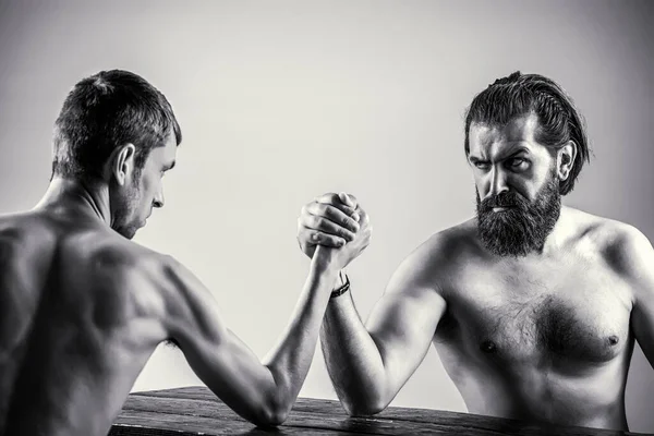 Arms wrestling thin hand, big strong arm in studio. Two mans hands clasped arm wrestling, strong and weak, unequal match. Black and white — Stok Foto