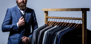 Erkek kıyafeti, atölyesinde terzi. Erkek takımları peş peşe asılıyor. Erkek kıyafetleri, butikler. Terzi, terzilik. Şık erkek kıyafeti.