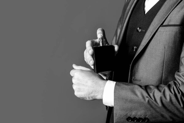 Fragrance smell. Men perfumes. Fashion cologne bottle. Man holding up bottle of perfume. Men perfume in the hand on suit background. Man in formal suit, bottle of perfume, closeup