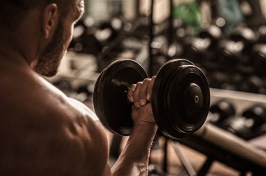 Spor salonunda dambılı kaldıran bir adam kas egzersizi yapıyor. Vücut geliştirici, spor salonunda halterlerle çalışıyor. Fitness adamı dambılı kaldırıyor.