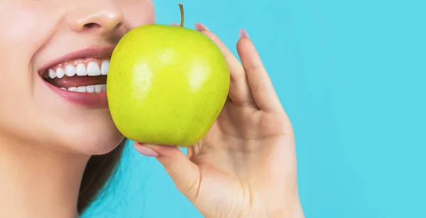 Концепция стоматологии. Женщина с идеальной улыбкой держит яблоко, синий фон. Женщина ест зеленое яблоко. Портрет молодой красивой счастливой улыбающейся женщины с зелеными яблоками. Здоровое питание — стоковое фото