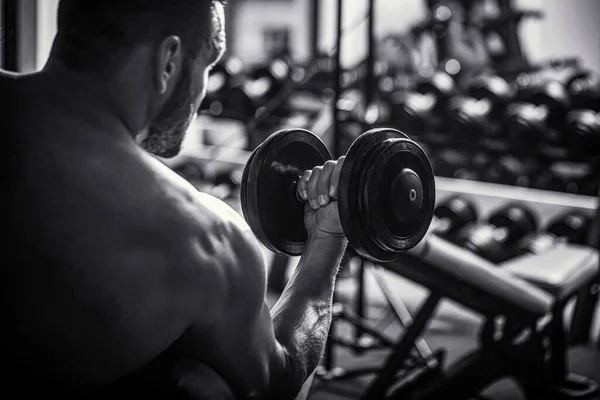 Culturista haciendo ejercicio con pesas de mancuerna en el gimnasio. Hombre culturista haciendo ejercicios con pesas —  Fotos de Stock