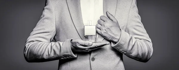 Fragrance smell. Men perfumes. Fashion cologne bottle. Man holding up bottle of perfume. Men perfume in the hand on suit background. Man in formal suit, bottle of perfume, closeup