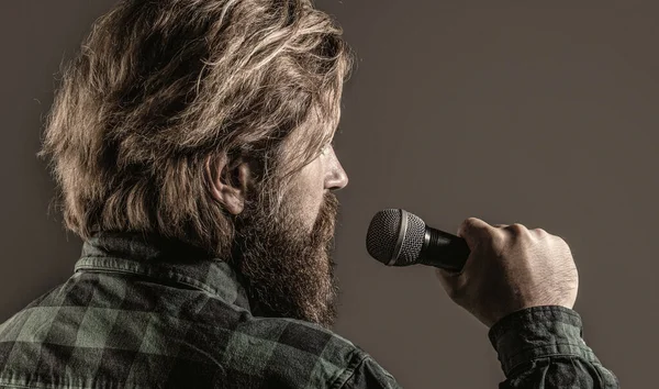 Un hombre con barba sosteniendo un micrófono y cantando. El barbudo del karaoke canta una canción en un micrófono. Hombre asiste al karaoke —  Fotos de Stock