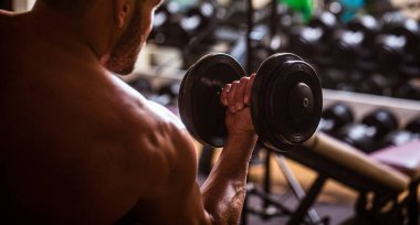 Vücut geliştirici, dambıllarla egzersiz yapıyor. Vücut geliştirici spor salonunda halterlerle çalışıyor.