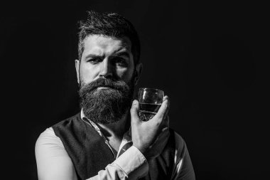 Man holding a glass of whisky. Sipping whiskey. Portrait of man with thick beard. Macho drinking. Degustation, tasting. Man with beard holds glass brandy. Black and white