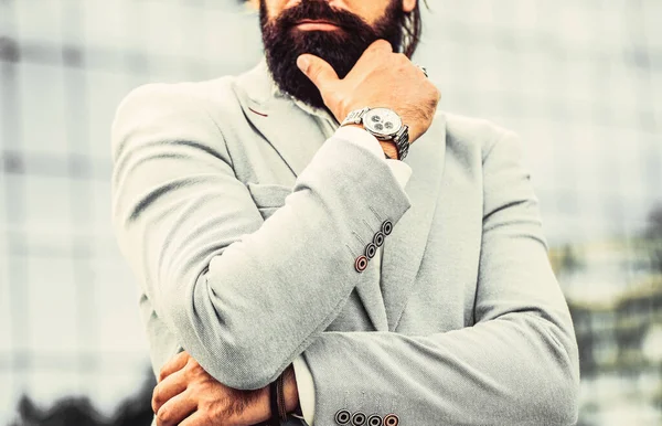 Portrait successful businessman in a business suit, using the watch on a city background. Watch in a man. Businessman points to his watch on the background of the town. The man holds his watch — Stock Photo, Image