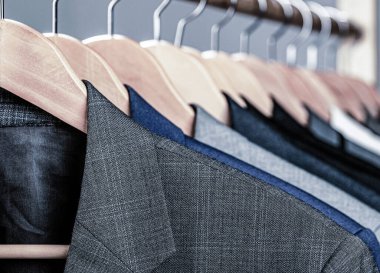 Perakende giyim mağazasında askıda asılı farklı renklerde erkek giysileri, yakın plan. Erkek gömlekleri, takım elbise askıda asılı. Butikte üzerinde ceket olan askılar. Askıda asılı erkekler için takım elbiseler