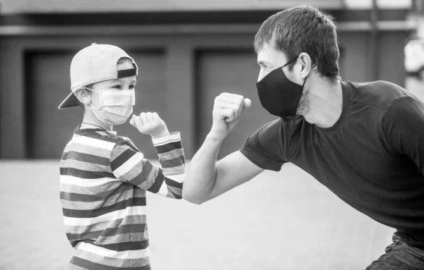 Father puts her son a face protective mask outdoors. Father and son bump elbows outdoors. Coronavirus quarantine. Black and white — Stock Photo, Image