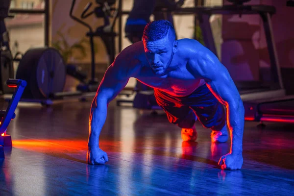 Masculino haciendo flexiones. Un hombre delgado haciendo flexiones en el gimnasio. Hombre haciendo flexiones. Hombre musculoso haciendo flexiones en una mano contra el fondo del gimnasio. Deporte. Musculoso y fuerte chico haciendo ejercicio — Foto de Stock