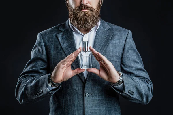Male holding up bottle of perfume. Man perfume, fragrance. Perfume or cologne bottle and perfumery, cosmetics, scent cologne bottle, male holding cologne. Masculine perfume, bearded man in a suit