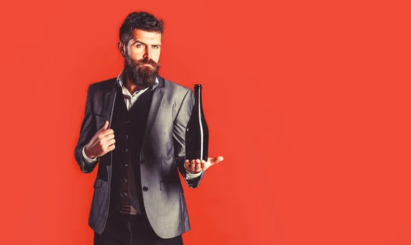 Hombre barbudo con una botella de champán y una copa. La persona sostiene una botella de vino tinto en una mano. Elegante hombre en esmoquin, traje, chaqueta —  Fotos de Stock