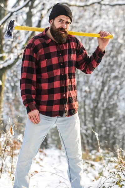 Lumberjack in the woods with an ax. Brutal bearded man with beard and moustache on winter day, snowy forest. Handsome man, hipster, lumberjack
