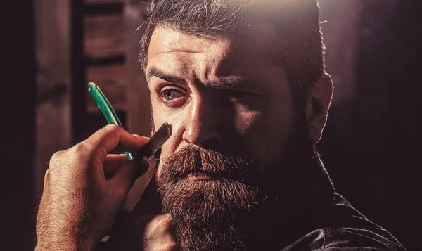 Navaja de afeitar vintage. Corte de pelo para hombre. Un hombre en la barbería. Guapo peluquero barbudo está sosteniendo una navaja de afeitar recta mientras barbería —  Fotos de Stock