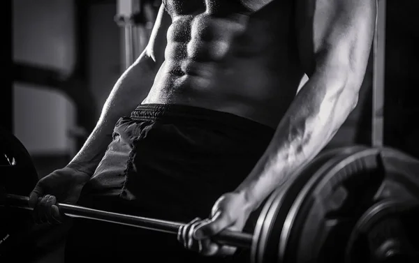 Hombre atlético con seis manadas, abdominales perfectos. Entrenamiento de primer plano de las barras del callejón sin salida. El deportista levanta la barra en el gimnasio. Entrenamiento de cerca con barra. Blanco y negro —  Fotos de Stock