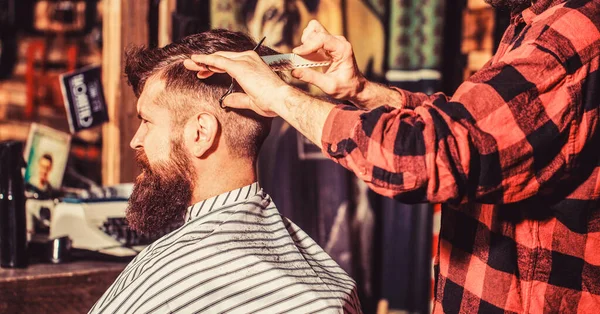 Hairdresser cutting hair of male client. Man visiting hairstylist in barbershop. Barber scissors. Bearded man in barber shop. Work in the barber shop. Man hairstylist