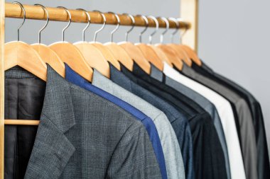 Perakende giyim mağazasında askıda asılı farklı renklerde erkek giysileri, yakın plan. Erkek gömlekleri, takım elbise askıda asılı. Butikte üzerinde ceket olan askılar. Askıda asılı erkekler için takım elbiseler