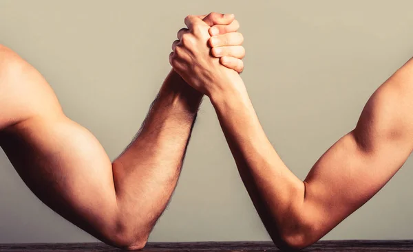 Arm wrestling thin hand and a big strong arm in studio. Two mans hands clasped arm wrestling, strong and weak, unequal match