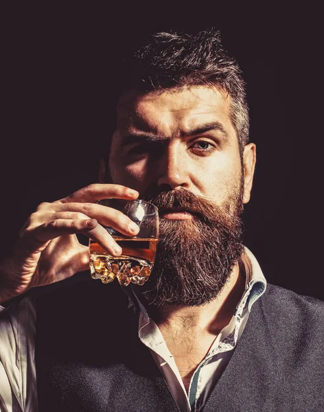 Whiskyt, brandyt, konyakot iszik. Degustáció, kóstolás. A szakállas férfi egy pohár brandyt tart a kezében. Kóstoló és elkorcsosító koncepció. Szakállas üzletember elegáns öltönyben, üveg whiskyvel. — Stock Fotó