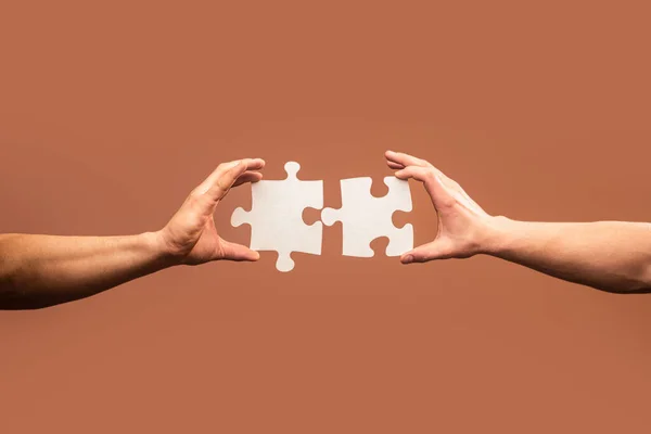 Holding puzzle. Business solutions, success and strategy concept. Two hands trying to connect couple puzzle piece on gray background. Teamwork concept. Closeup hand of connecting jigsaw puzzle