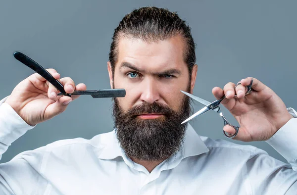 Tipo brutal, tijeras, navaja de afeitar. Cliente barbudo visitando peluquería. Tijeras de peluquero y navaja de afeitar, peluquería, traje. Peluquería vintage, afeitado. Hombre barbudo retrato. Hombres bigote —  Fotos de Stock