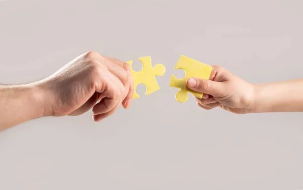 Puzzles. Hand of the child and hand of mother fold puzzle, closeup. Hands hold puzzles. Solution of problems. Mens and childs hands connecting puzzles. Hands connecting puzzle