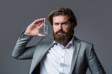 Erkek parfümü, takım elbiseli sakallı bir adam. Elinde parfüm şişesi tutan bir erkek. Erkek parfümü, parfüm. Parfüm ya da parfüm şişesi ve parfüm, kozmetik, parfüm şişesi, kolonya tutan erkek.
