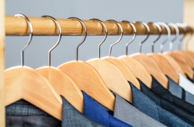 Askıda asılı erkekler için. Perakende giyim mağazasında askıda asılı farklı renklerde erkek giysileri, yakın plan. Erkek gömlekleri, takım elbise askıda asılı. Butikte üzerinde ceket olan askılar.