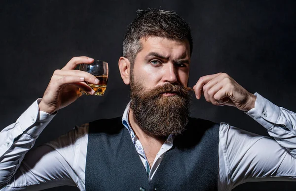 Omul cu barbă ţine pahar de coniac. Conceptul de degustare și degustare. Omul de afaceri cu barbă în costum elegant, cu pahar de whisky. Un om care bea whisky, coniac, coniac. Degustare, degustare — Fotografie, imagine de stoc