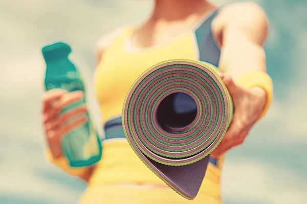 Kobieta w sportowym stroju trzyma matę do jogi i butelkę wody. Mata do jogi i butelka wody. Koncepcja zdrowego stylu życia. Zbliżenie — Zdjęcie stockowe