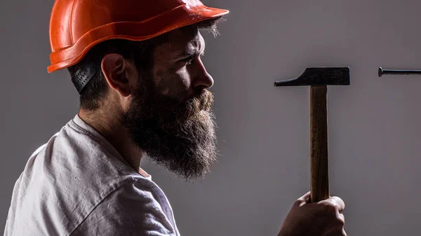 Hamer die een spijker hamert. Handyman diensten. Bouwers met een helm, helm. Een man met baard, helm, helm, hoed. Handyman, hamer, man bouwer, industrie, technologie — Stockfoto