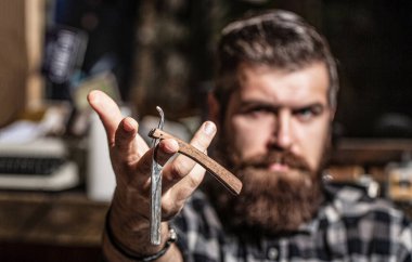 Düz tıraş bıçağı, berber dükkanı, sakal. Vahşi sakallı adamın portresi. Klasik düz tıraş bıçağı. Erkek tıraşı. Berber dükkanındaki adam. Yakışıklı sakallı kuaför berber dükkanı işletirken elinde jilet tutuyor.