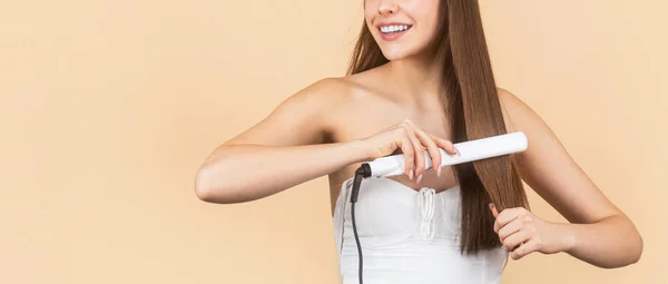 Donna raddrizzante per capelli con piastra. Ritratto di giovane bella ragazza che usa lo styler sui suoi capelli lucenti. Acconciatura. Bella donna sorridente stiratura capelli lunghi con ferro piatto — Foto Stock