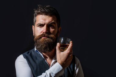 Elinde bir bardak viski tutan bir adam. Viski yudumluyor. Kalın sakallı bir adamın portresi. Maço içki. Sakallı adam cam brendi tutuyor..