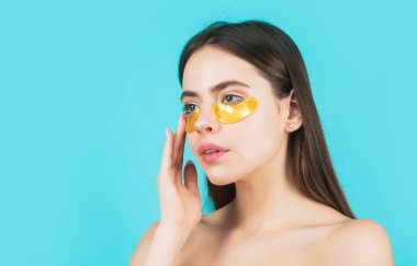 Altın göz bandı yapıştıran bir kadın. Portre kızı yakın plan. Göz bantlı güzel kadın portresi mükemmel bir cilt etkisi gösteriyor. Göz maskeli kozmetik bantlar. Kadının yüzü yakın plan.