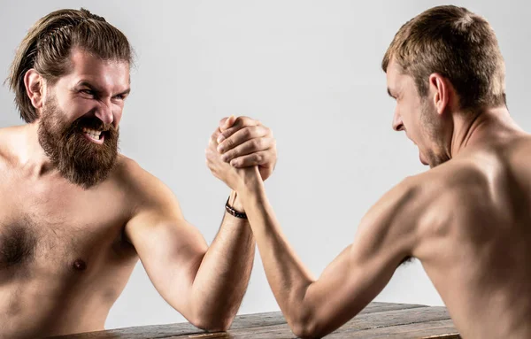 Heavily muscled bearded man arm wrestling a puny weak man. Arms wrestling thin hand, big strong arm in studio. Two mans hands clasped arm wrestling, strong and weak, unequal match