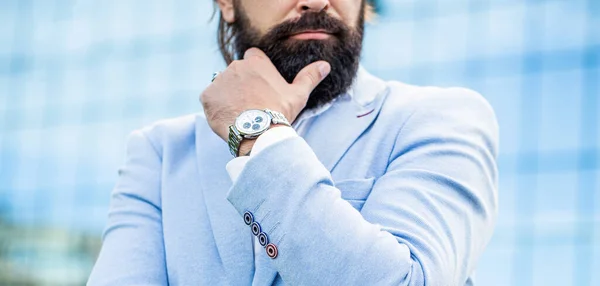 El hombre sostiene su reloj. Retrato exitoso hombre de negocios en un traje de negocios, utilizando el reloj en un fondo de la ciudad — Foto de Stock