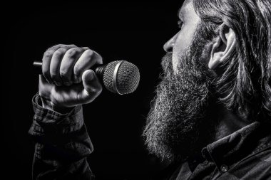 Man with a beard holding a microphone and singing. Bearded man in karaoke sings a song into a microphone. Male attends karaoke. Black and white