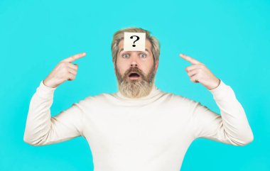 Sakallı adamın kafasında soru işareti, çözüm problemleri. Mavi arka planda soru işareti olan düşünen bir adam. Alnında soru işareti olan adam yukarı bakıyor. Soru işaretli kağıt notlar