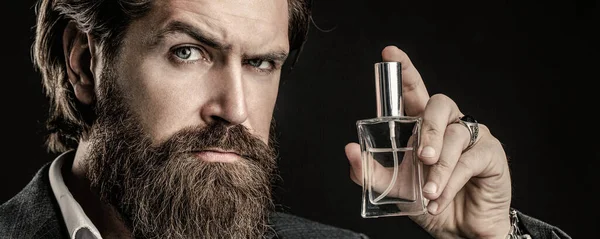 Маскулінна парфумерія, бородатий чоловік у костюмі. Чоловік тримає пляшку парфумів. Чоловічий парфум, аромат. Парфуми або одеколонова пляшка, парфумерія, косметика, пляшка аромату одеколону, чоловік тримає одеколон — стокове фото